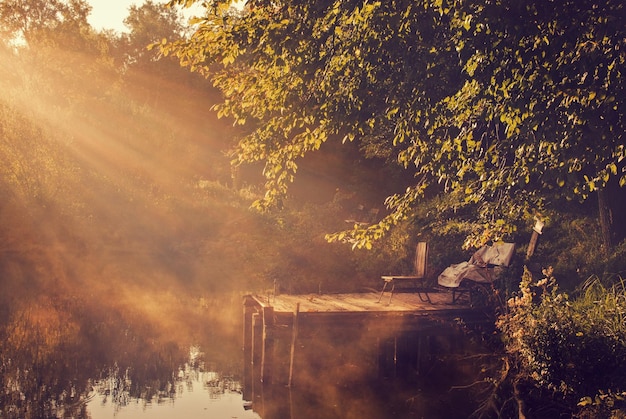 chairs on pier over lake in forest during sunset