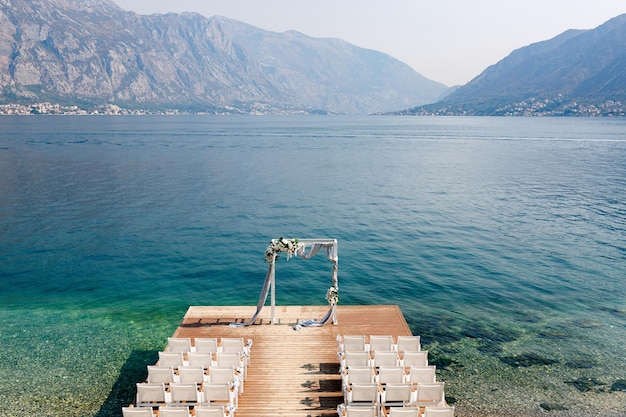 Chairs on the wooden pier in front of the wedding arch against the backdrop of the sea