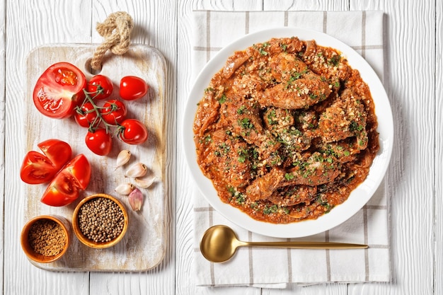 Chakhokhbili stewed chicken tomato with fresh herbs walnuts and spices on a white plate on a wooden table georgian cuisine flat lay