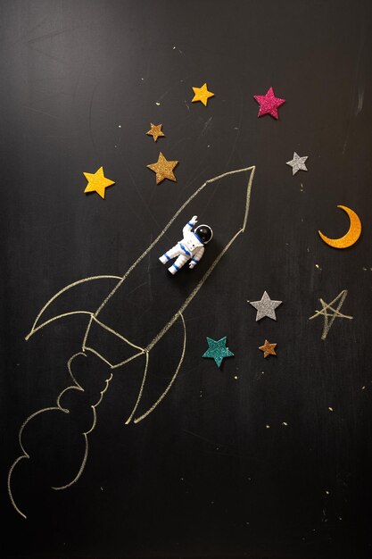 Photo chalk drawing rocket with toy astronaut on blackboard going up quickly