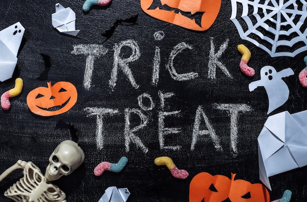 Chalk lettering Trick or Treat on a chalk board with handmade Halloween decor and skeleton, gummy worms. Halloween theme