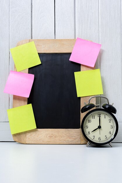 Chalkboard, Alarm clock and blank sticky note, post note on Office desk white wooden backg