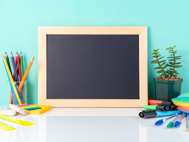 Chalkboard and school supplies on white table by the blue wall. Side view, empty. 