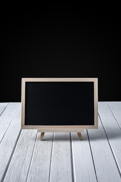 The chalkboard on the stand on wooden floor and black background