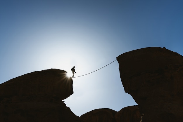課題、リスク、集中力、そして勇気の概念。絶壁の上をロープで歩く人バランスをシルエットします。