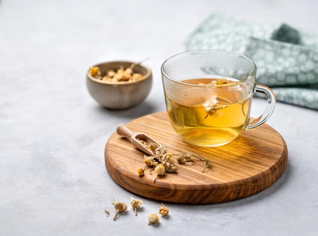 Chamomile herbal tea in a glass cup on a wooden board on a light background with dry flowers The concept of a healthy detox drink for health and sleep