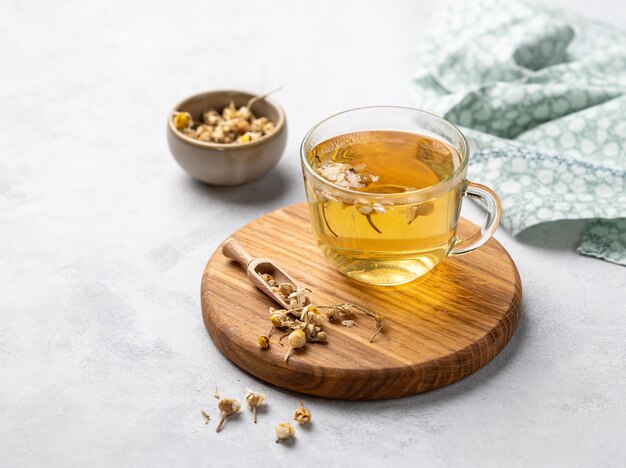 Chamomile herbal tea in a glass cup on a wooden board on a light background with dry flowers The concept of a healthy detox drink for health and sleep