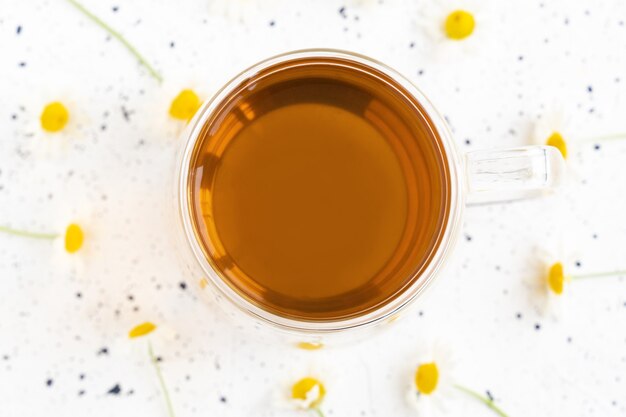 Chamomile tea and chamomile in glass mug on white cement table. Herbal tea. Top view. Flat lay.