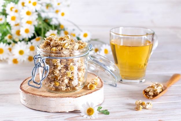 Chamomile tea in the jar on the white wooden table. Dried and Fresh Flowers