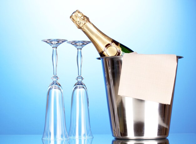 Champagne bottle in bucket with ice and glasses on blue background