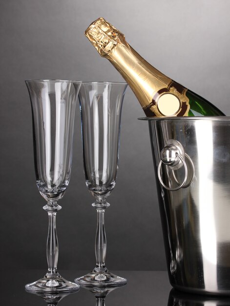 Champagne bottle in bucket with ice and glasses on grey background