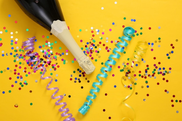 Champagne bottle and confetti with streamer on yellow background