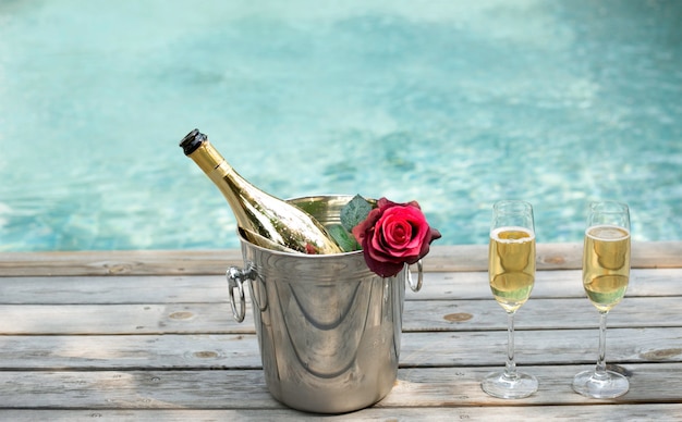 Photo champagne bottle in ice bucket and champagne glass by swimming pool