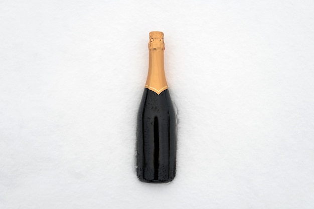 Champagne bottle in the snow. Green closed bottle without a label.