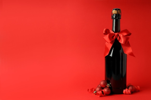 Champagne bottle with bow, and baubles on red background.