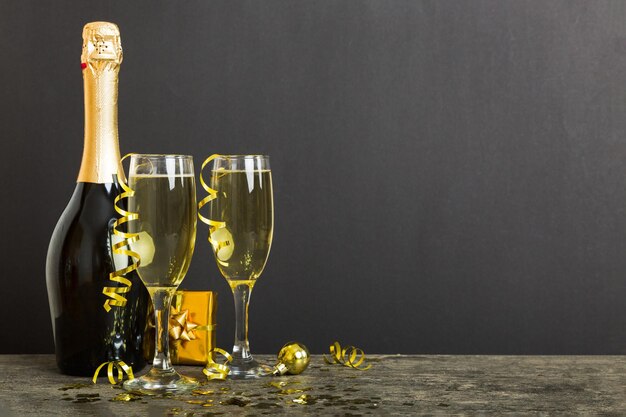 Champagne bottle with confetti glasses and christmas decor on colored holiday background Flat lay New Year decorations