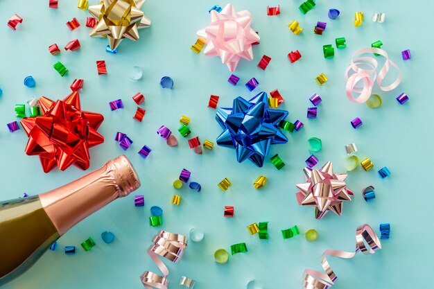 Бутылка шампанского с праздничным украшением конфетти и партийными растяжками на синем праздничном фоне. Рождество, день рождения или свадьба концепция. Плоская планировка.