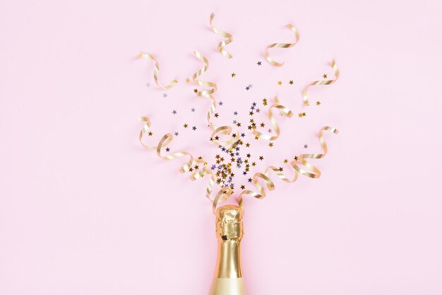 Champagne bottle with confetti stars and party streamers on pink background Christmas birthday or