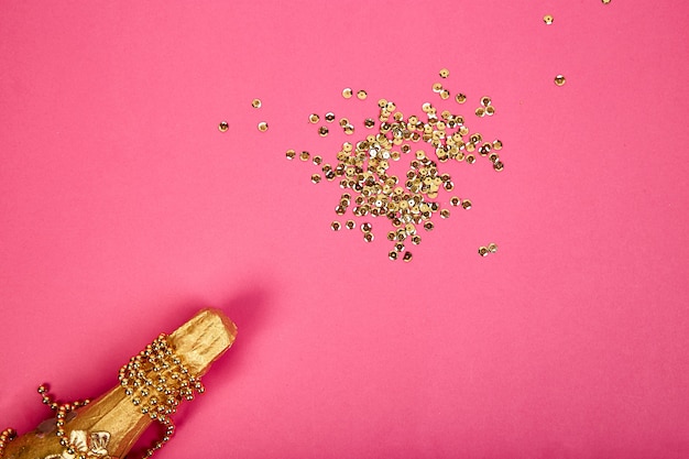 Champagne bottle with golden confetti on pink paper background.