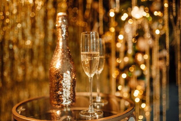 Champagne bottle with golden sequin and glasses at sparkling bokeh yellowish garlands