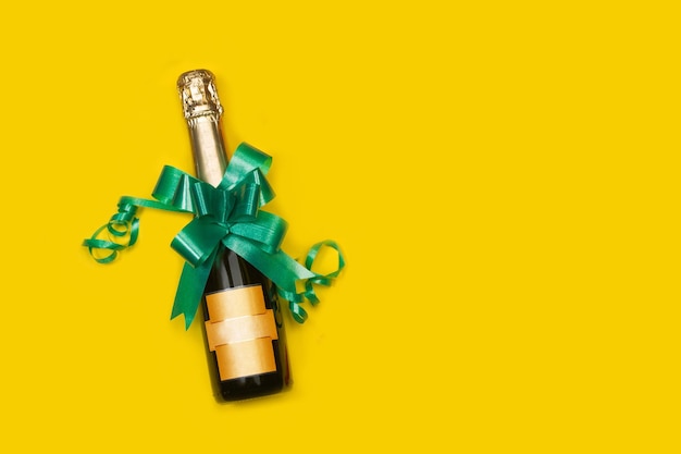 Champagne bottle with a green bow tie on a yellow background with copy space