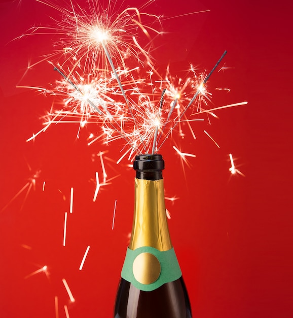 Champagne bottle with sparklers on red background. Flat lay.