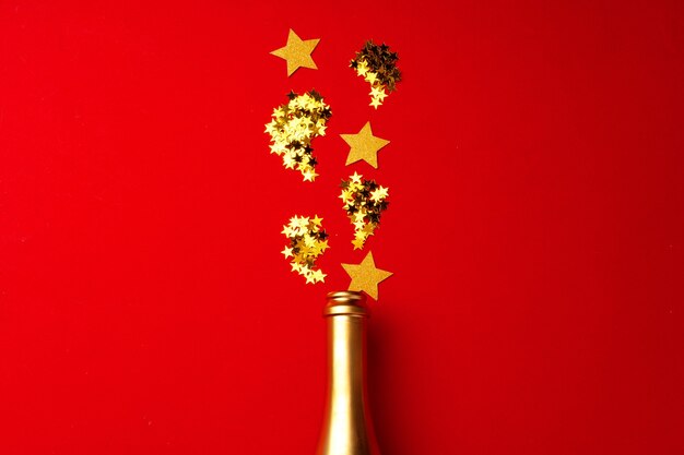 Champagne bottle with sparkling confetti on red
