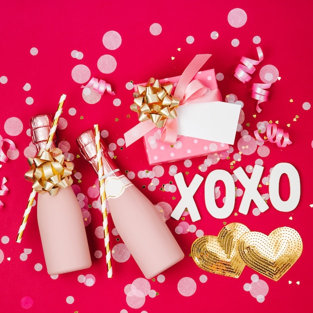 Champagne bottles with confetti and tinsel on red background. Valentines day or birthday party concept theme. Flat lay, top view