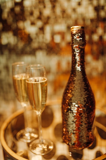 Foto champagne fles met gouden sequins en glazen met glinsterende bokeh geelachtige kralen