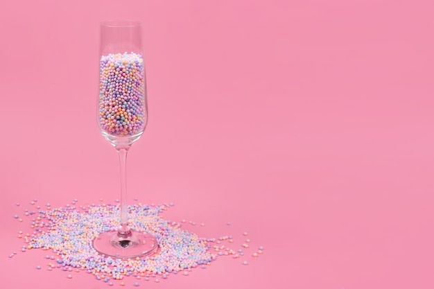 Champagne glass filled with colorful sugar balls on pink