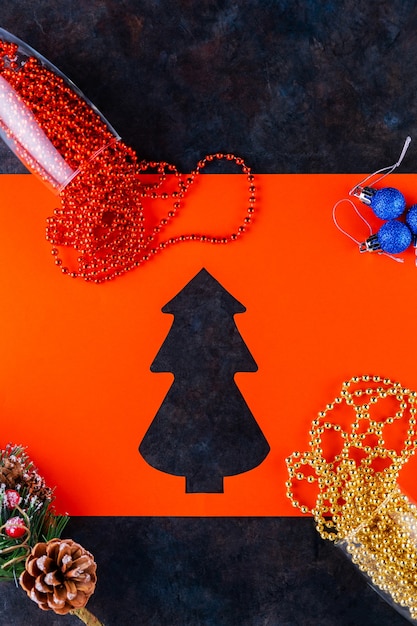 Фужеры с рождественскими бусами на темном фоне. Елочные шары, разноцветные бусы и еловая ветка. Рождественская елка вырезки из бумаги. Вид сверху