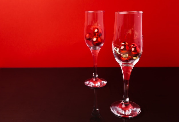 Champagne glasses with small Christmas balls inside against red background