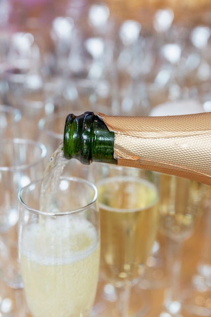 Champagne is poured into a glass on the buffet table. Close-up. Vertical.