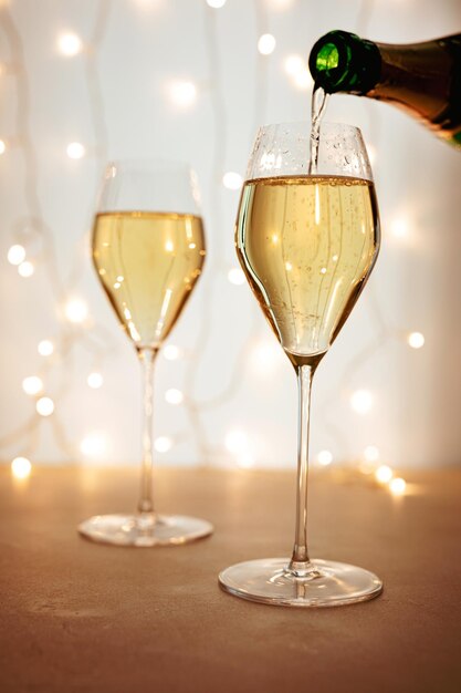 Champagne of mousserende wijn in een fluitglas gieten, bokehlichten op de achtergrond, kerst- of nieuwjaarsvakantiesfeer