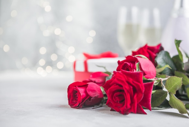 Champagne and red roses with bokeh. Valentine's setting with red roses and present