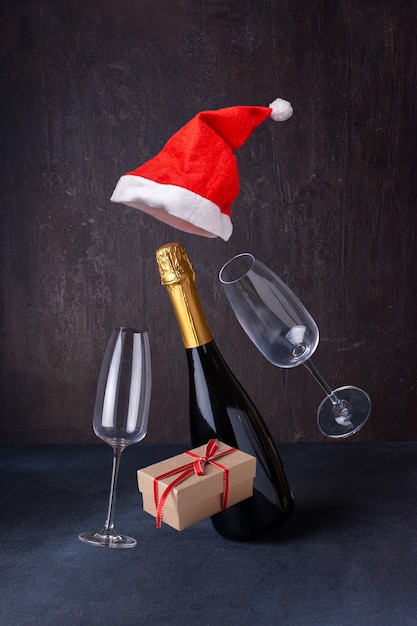 Foto champagne in cappello di babbo natale cibo volante, coriandoli su sfondo scuro