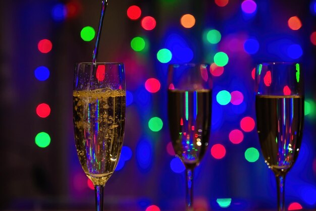 Foto champagne wordt in hoge glazen gegoten veelkleurige kerstverlichting op de achtergrond feestelijke stemming