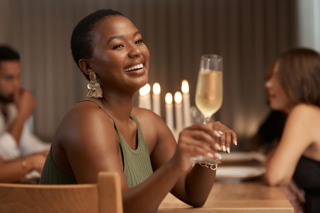 Champagnefeest en gelukkige zwarte vrouw op een feest of diner aan een tafel in de eetkamer Geluksglimlach en Afrikaanse dame genietend van een glas alcoholische drank tijdens een nieuwjaarsevenement in een huis