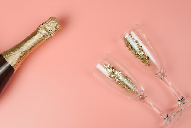 Champagnefles en wijnglazen met gouden confetti op een roze pastel