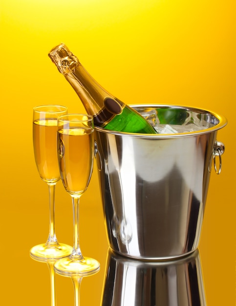 Champagnefles in emmer met ijs en glazen champagne, op gele achtergrond