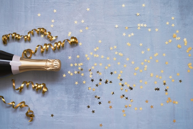Champagnefles met confetti sterren en feestwimpels op blauwe achtergrond kopie ruimte bovenaanzicht plat