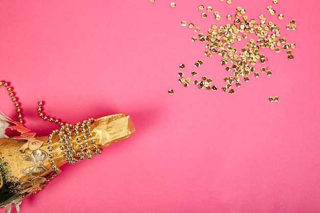Champagnefles met gouden confetti op roze papier achtergrond.