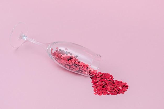 Champagneglas gevuld met confetti in de vorm van harten op het roze achtergrond zijaanzicht
