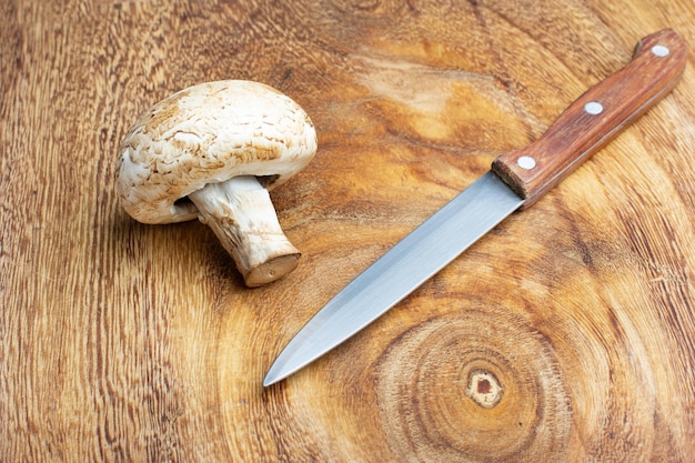 A champignon and a kitchen knife on a wooden table in a top view