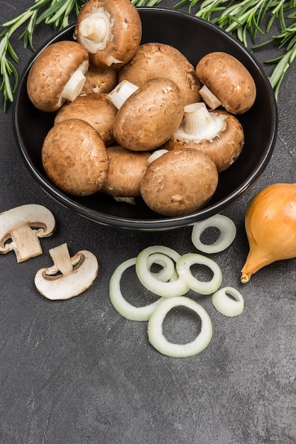 Шампиньоны в черной миске, нарезанный лук и грибы с веточками розмарина