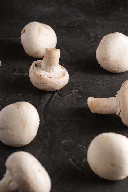 Champignon mushrooms healthy food on dark black textured background, angle view selective focus