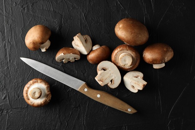 Champignon mushrooms and knife on black, top view