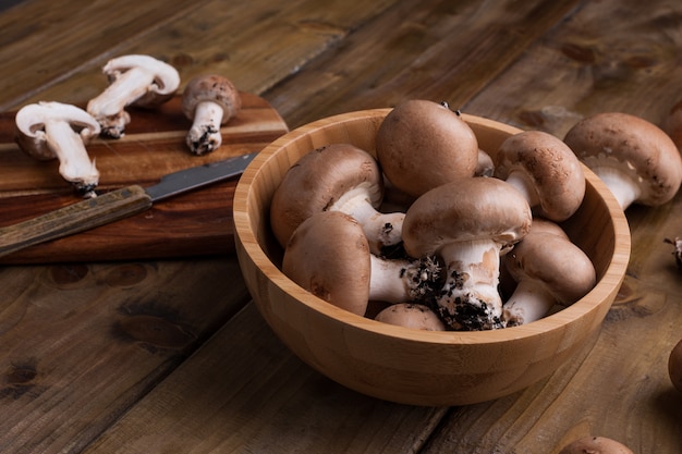 Champignon mushrooms in a wooden bowl and a knife with a board.