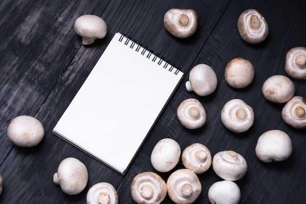 champignon paddestoelen op de houten zwarte tafel en schrijfblok