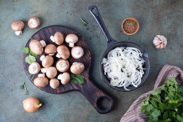 Foto i champignoni giacciono sulla tavola da taglio accanto a una padella piena di cipolle tritate